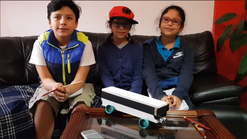Three students from the Mexico lab smile with their robotic bus on the table in front of them